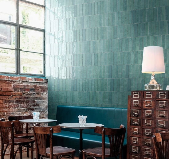 Restaurant interior with teal tiled walls, wooden chairs, and a lamp.
