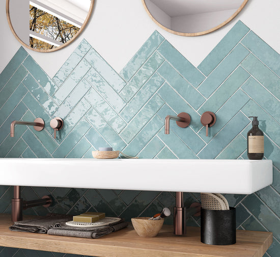 Bathroom with teal herringbone tiles, white sink, and wooden shelf.