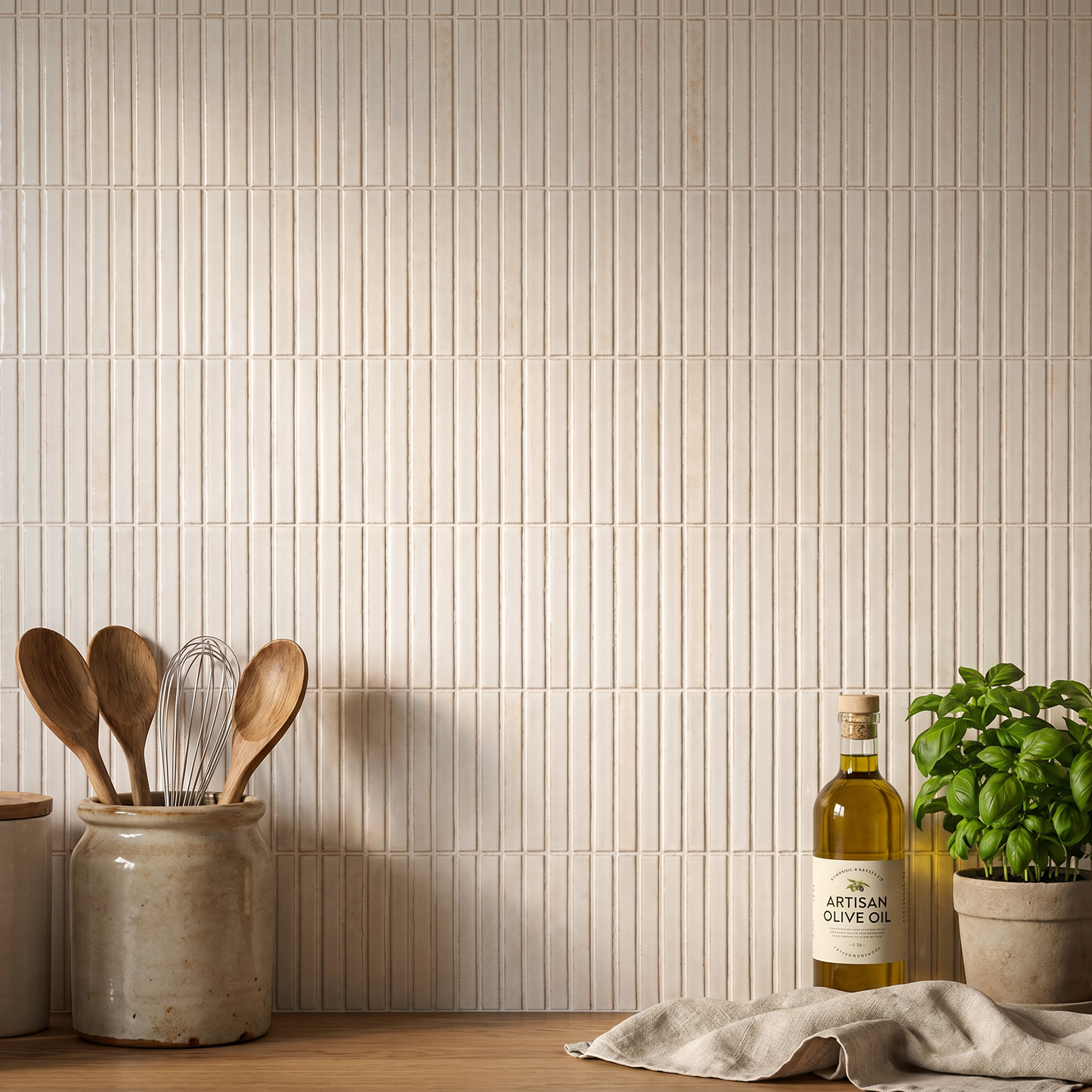 Kitchen scene with a bottle of Artisan Olive Oil, wooden utensils, and a plant against a tiled wall.